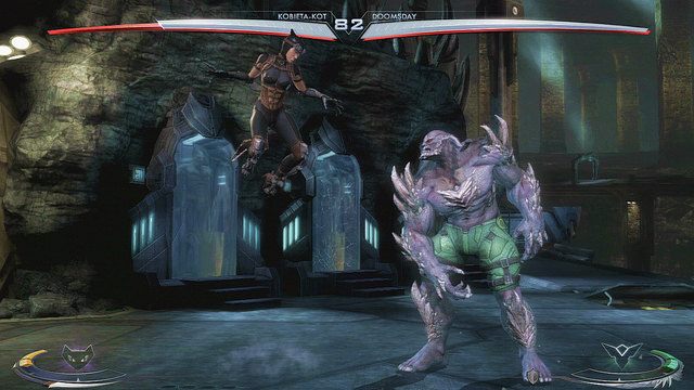 Po lewej stronie areny w tle znajdują się kostiumy Batmana w szklanych gablotach - Injustice: Jaskinia Batmana - arena - Injustice Gods Among Us - poradnik do gry